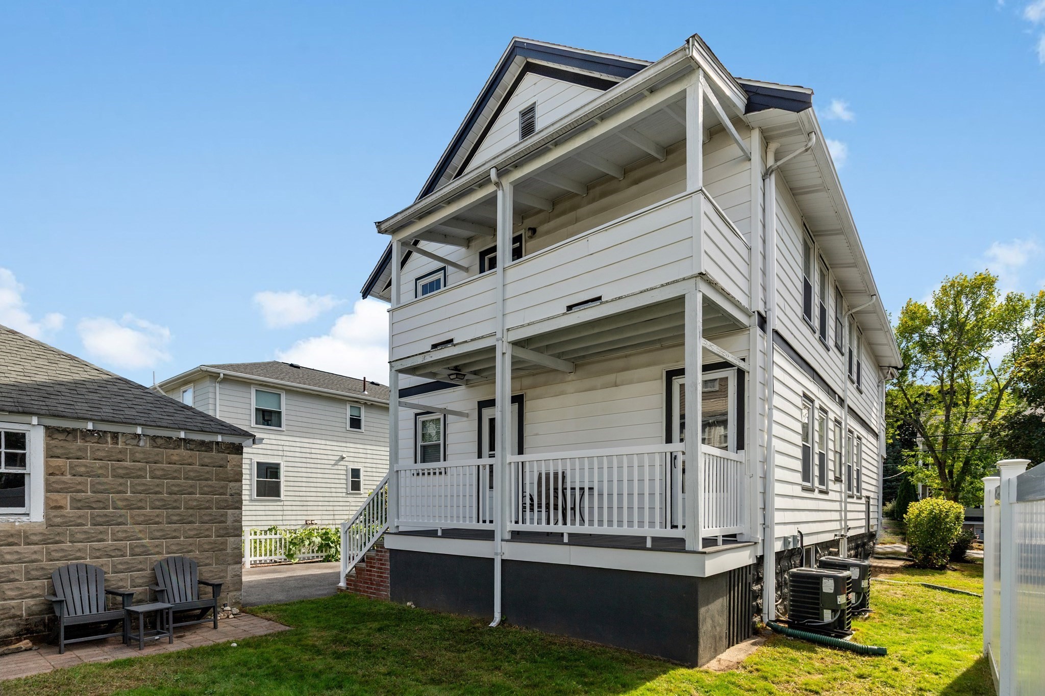White two-story house with stacked covered porches, white railings, and outdoor air-conditioning units.