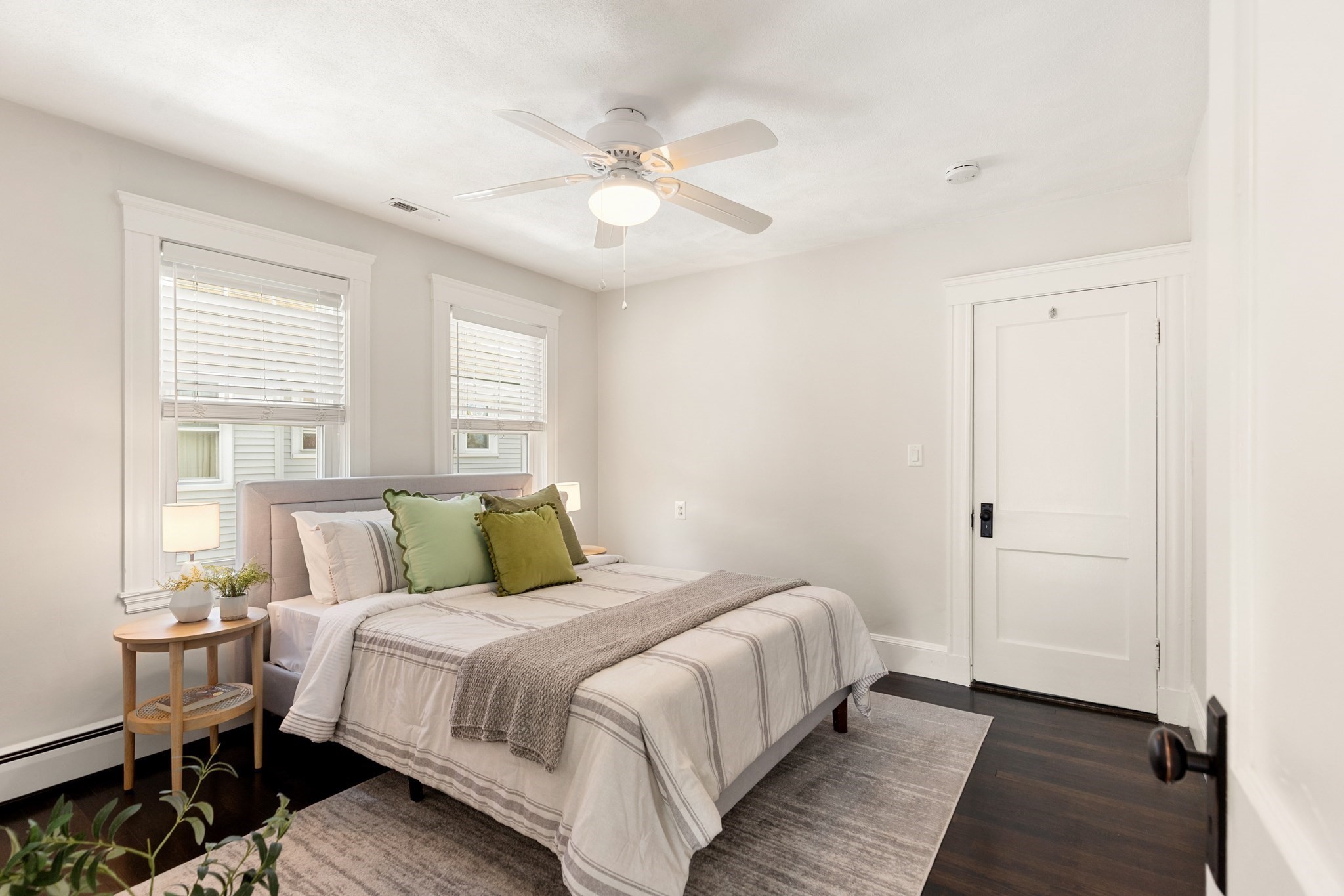 Bedroom with a bed, green accent pillows, two windows, and a ceiling fan.