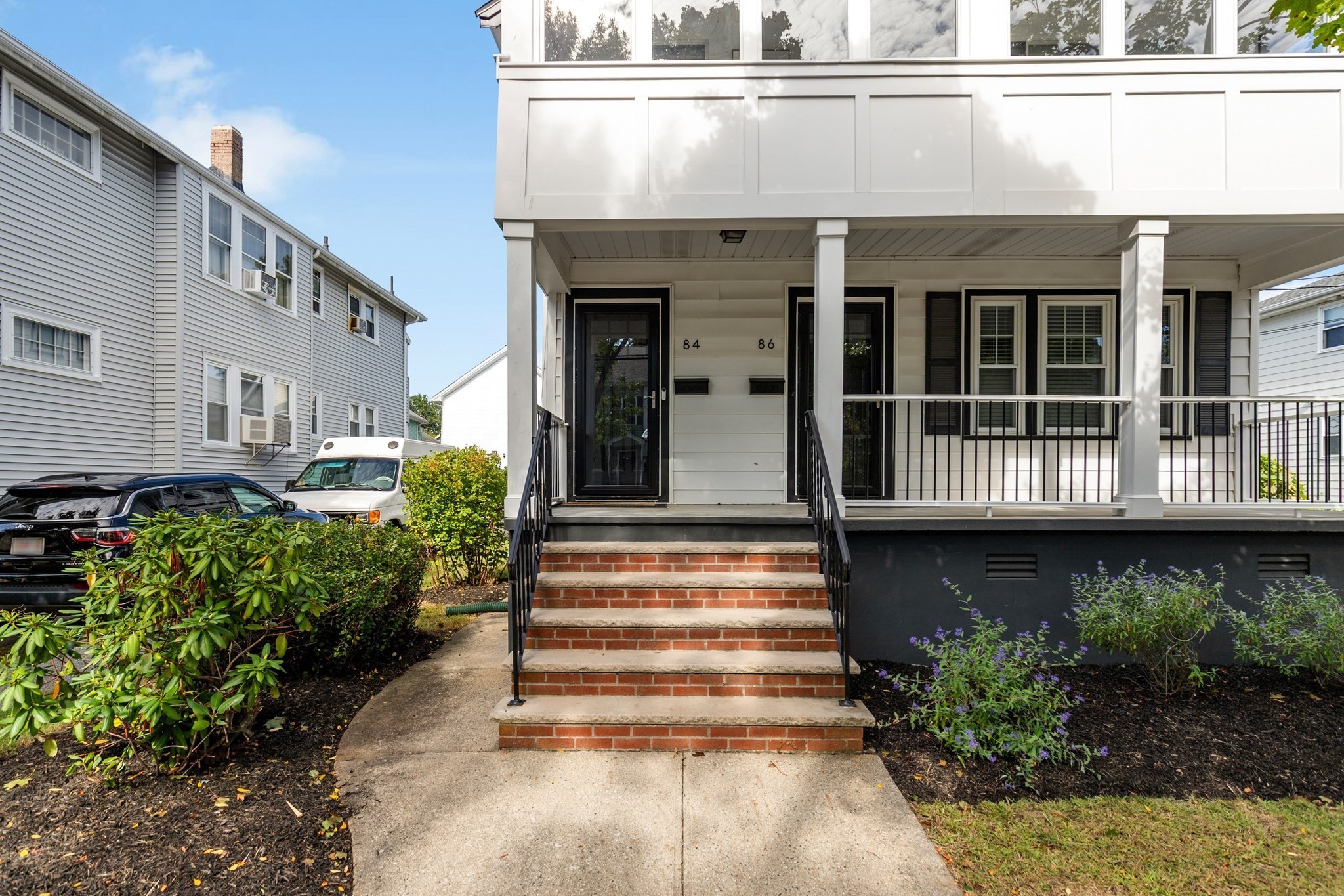 White multi-unit home with a covered porch, brick steps, and entrances numbered 84 and 86.