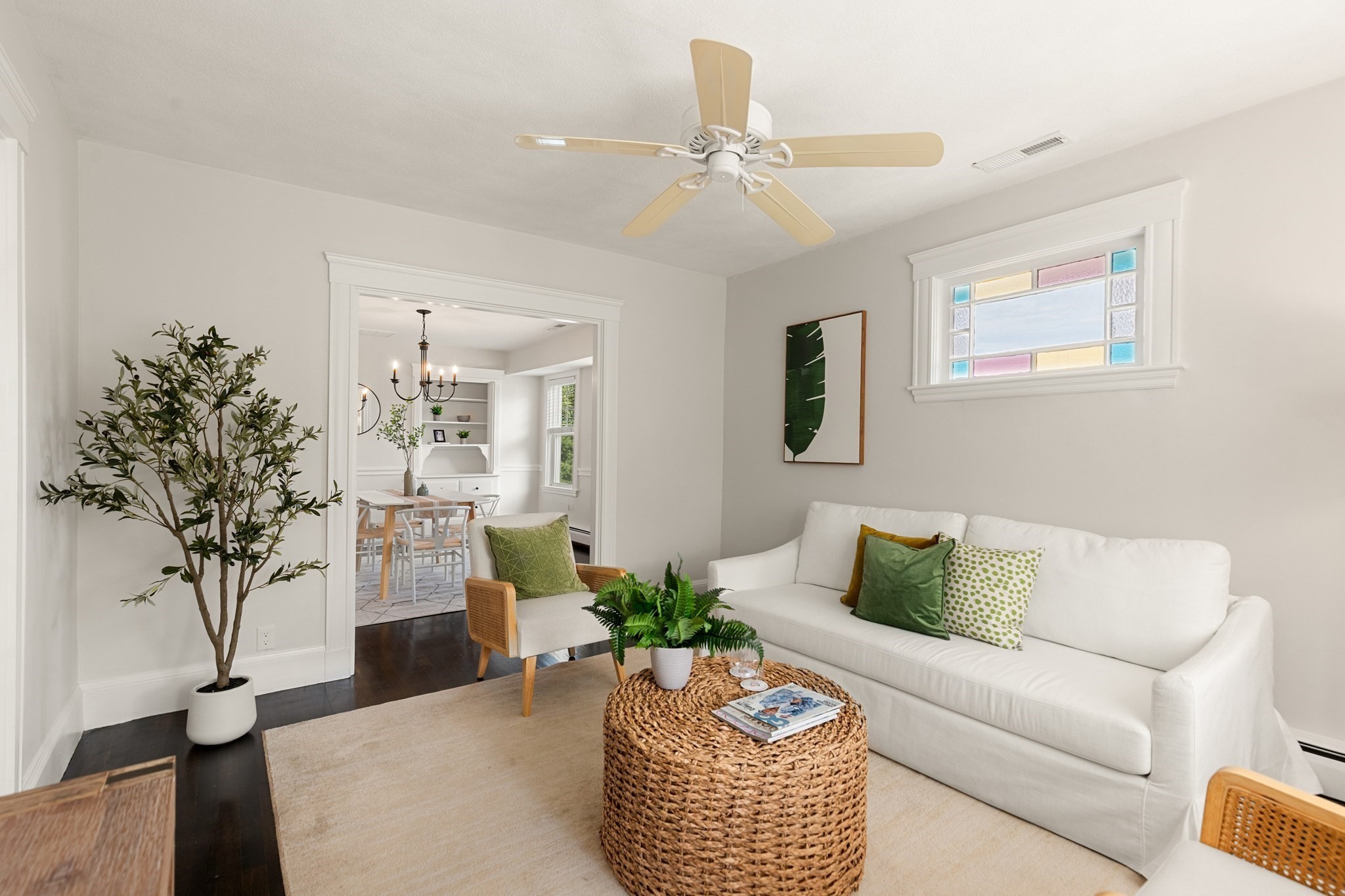 Staged living room with a white sofa, woven coffee table, and a colorful stained-glass window.