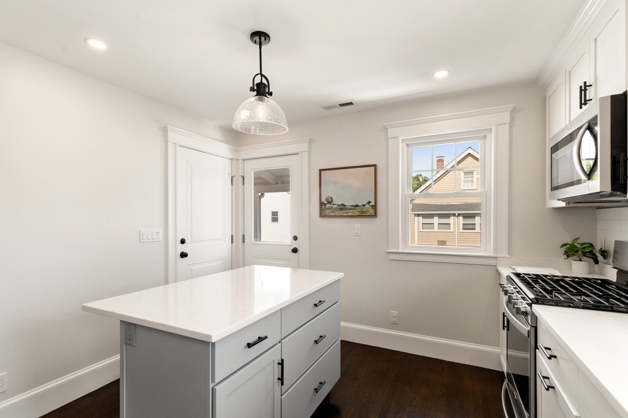 Bright kitchen with a white island, stainless steel appliances, and a window beside a glass-paneled door.
