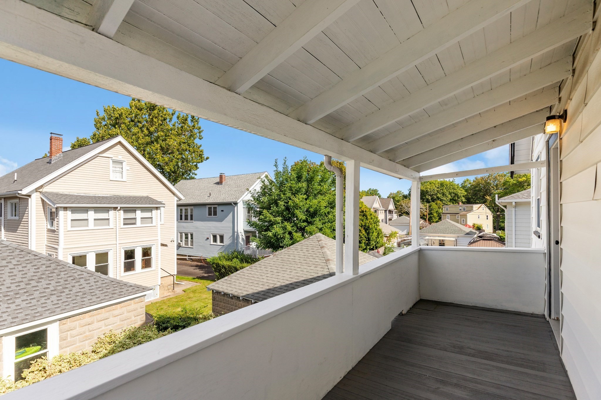Covered porch overlooking neighboring homes and leafy trees.