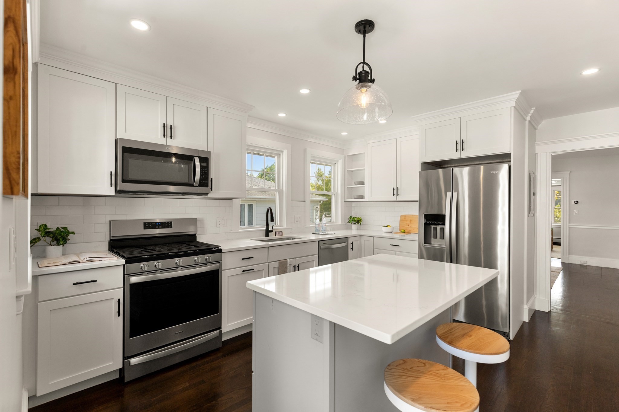 Bright white kitchen with stainless steel appliances, a large island, and two wood-topped stools.