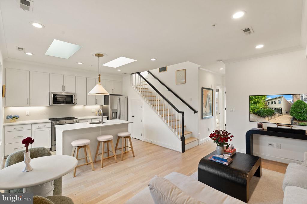 Open-plan kitchen and living area with a white island, stainless steel appliances, and a black-railed staircase.