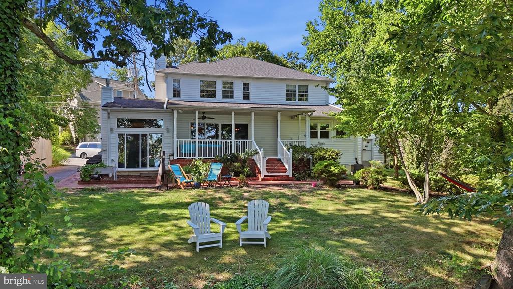 Two-story white house with a covered porch, backyard lawn, and Adirondack chairs.