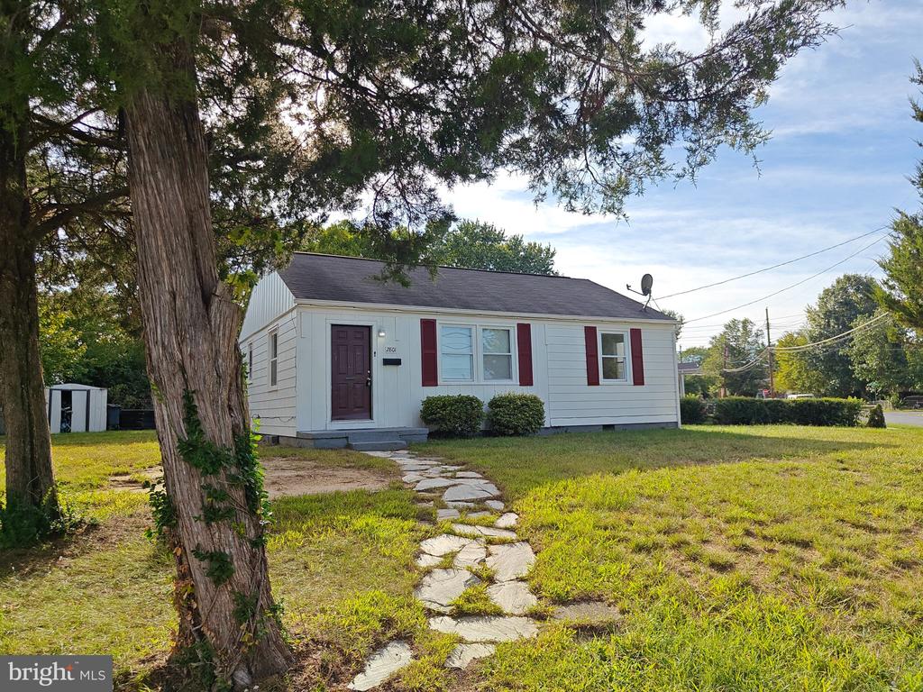 Single-story white house with red shutters behind a stone walkway and large mature tree.