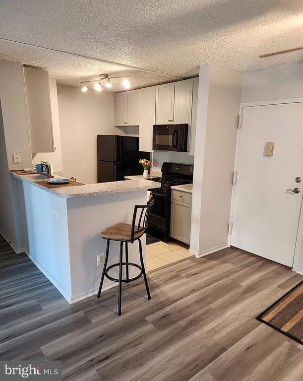 Compact kitchen with white cabinets, black appliances, a breakfast peninsula, and gray wood-look flooring.