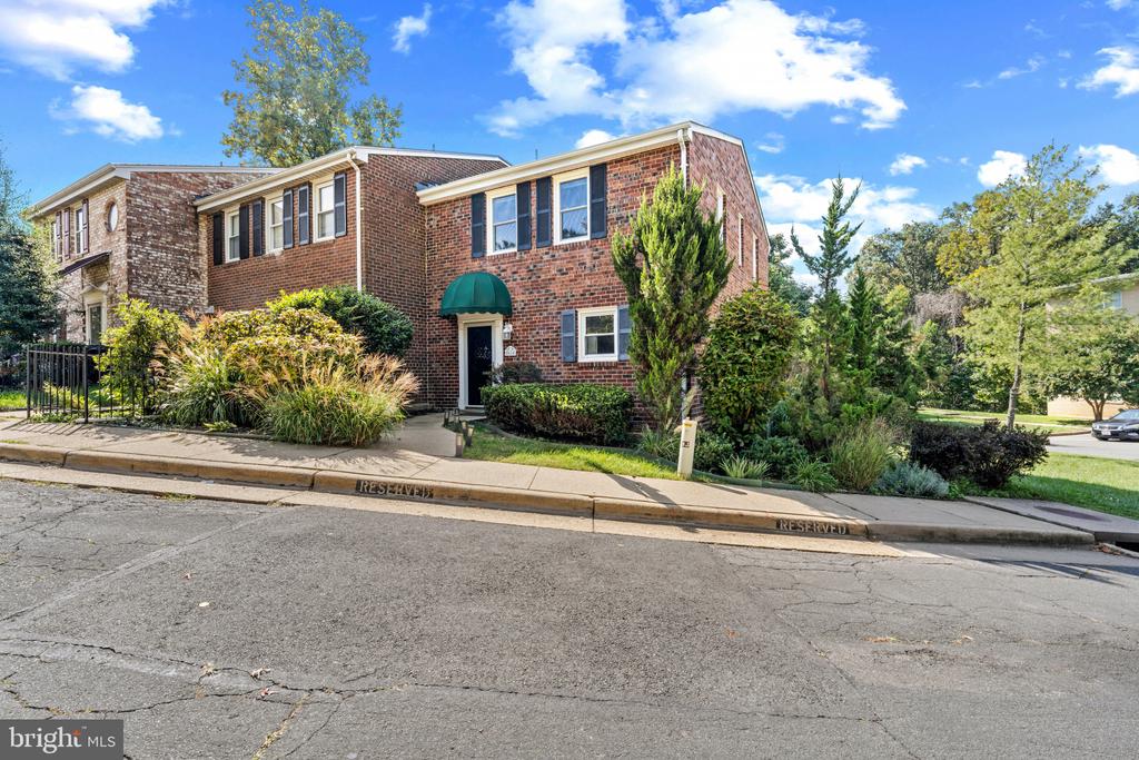 Two-story red-brick home with dark shutters, a green entry awning, and mature landscaping.
