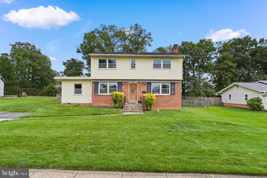 Two-story cream-sided and brick house with a broad green front lawn.