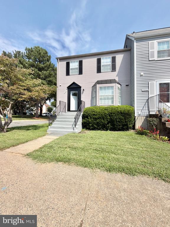 Gray-sided attached home with a bay window, front steps, and lawn.