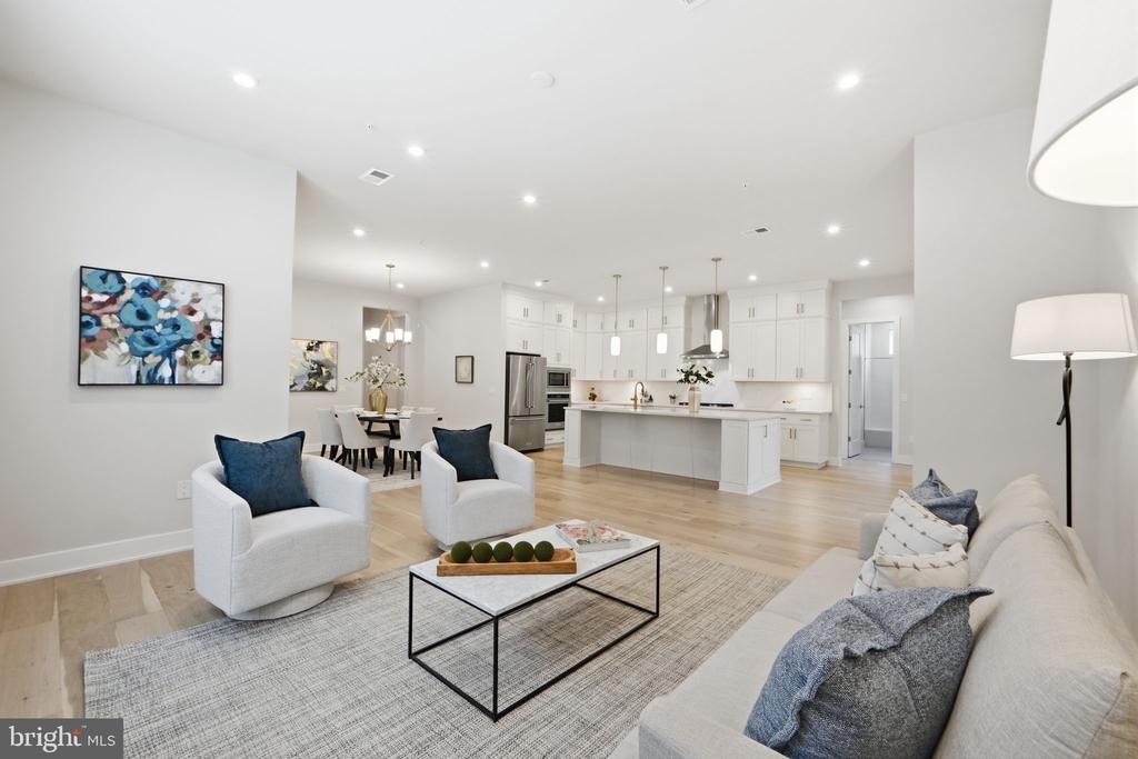 Open-plan living room and kitchen with white cabinetry, pale wood floors, and blue accent pillows.