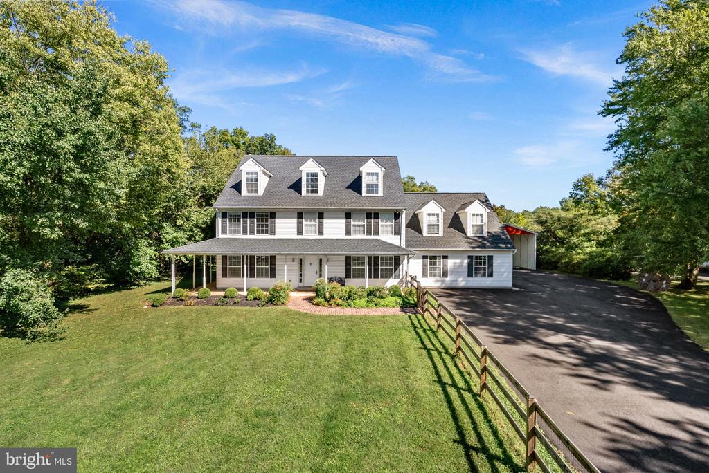 Large white two-story home with dormer windows, a wraparound porch, and a tree-lined lawn.