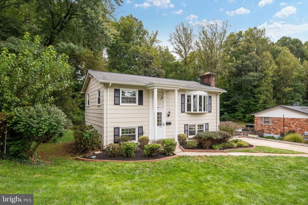 Beige split-level home with dark shutters, brick chimney, landscaped foundation, and green lawn.