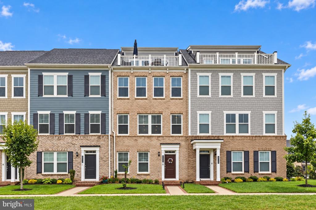 Three-story attached townhouses with varied façades, rooftop railings, and landscaped front lawns.