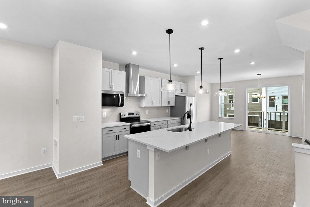 Vacant kitchen with white cabinets, stainless appliances, and a large island beneath pendant lights.