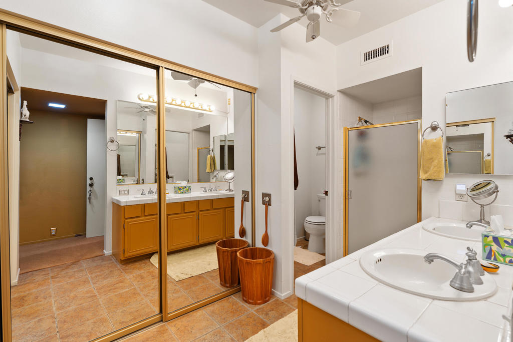 Bathroom with a double-sink vanity, orange cabinetry, mirrored sliding doors, and terracotta-colored tile flooring.