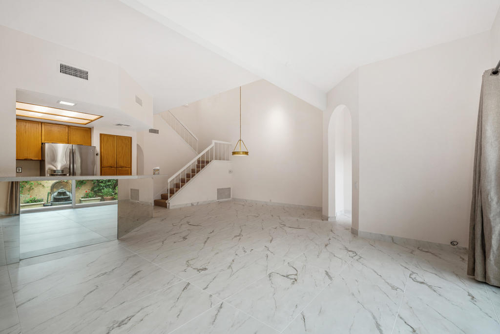 Vacant living area with marble-look tile, a staircase, and an open kitchen with wood cabinets.