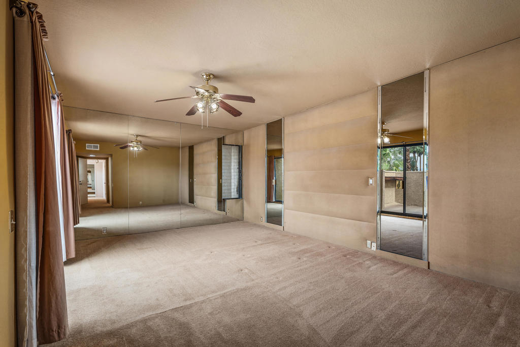 Vacant bedroom with mirrored walls, beige carpet, and a ceiling fan.