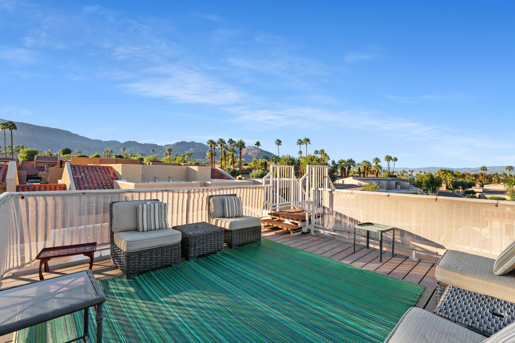 Furnished rooftop patio with mountain views, wicker seating, and a green striped rug.