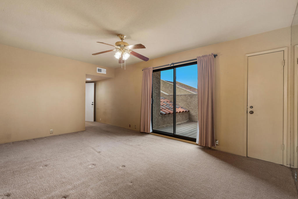 Empty carpeted bedroom with a ceiling fan and sliding glass door to a patio.
