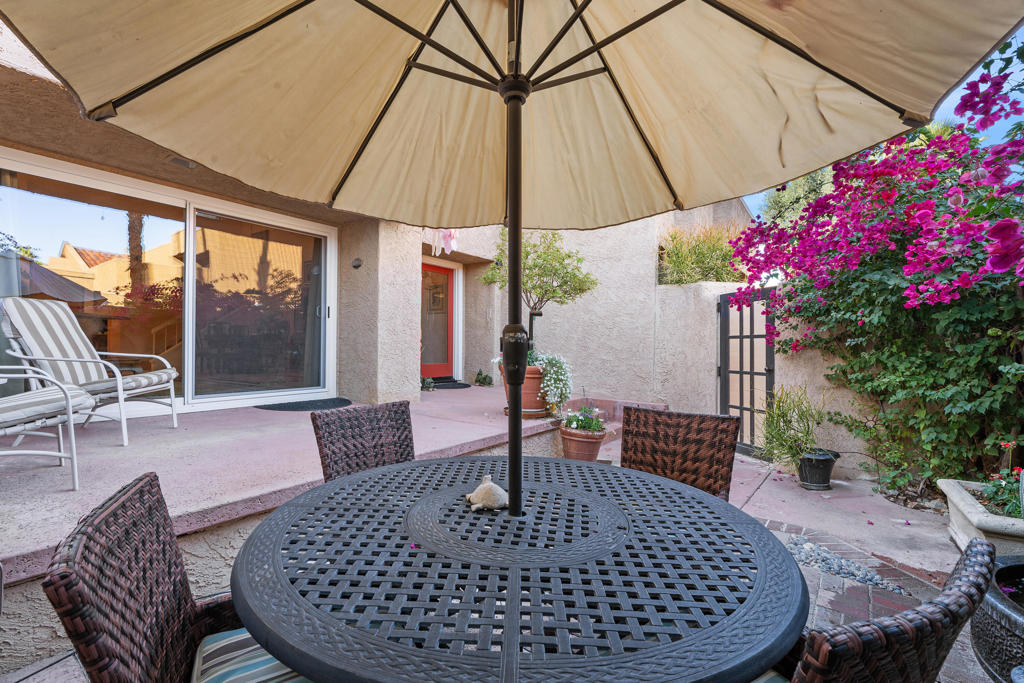 Furnished patio with a large umbrella over a round table, woven chairs, and flowering bougainvillea.