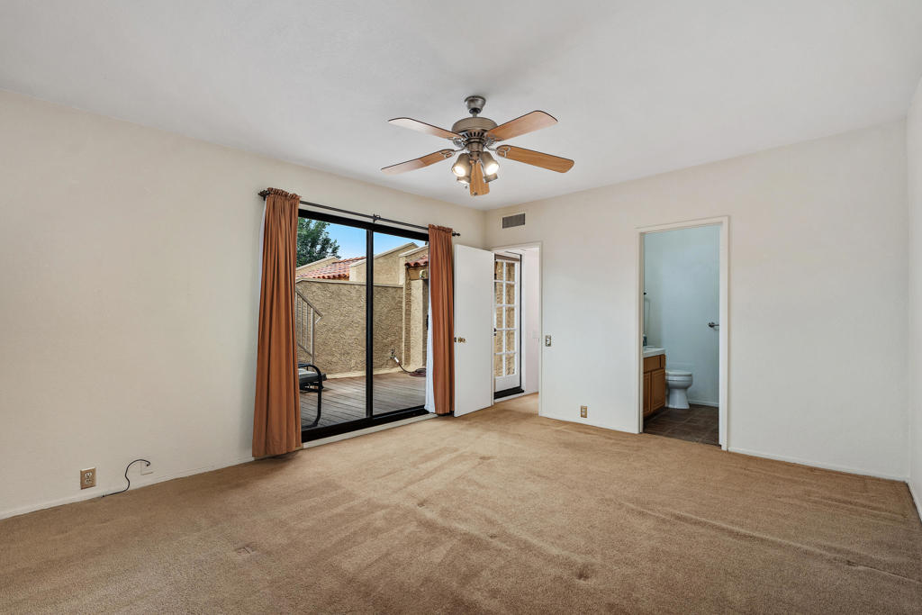 Empty carpeted bedroom with a ceiling fan and sliding glass doors opening to a patio.