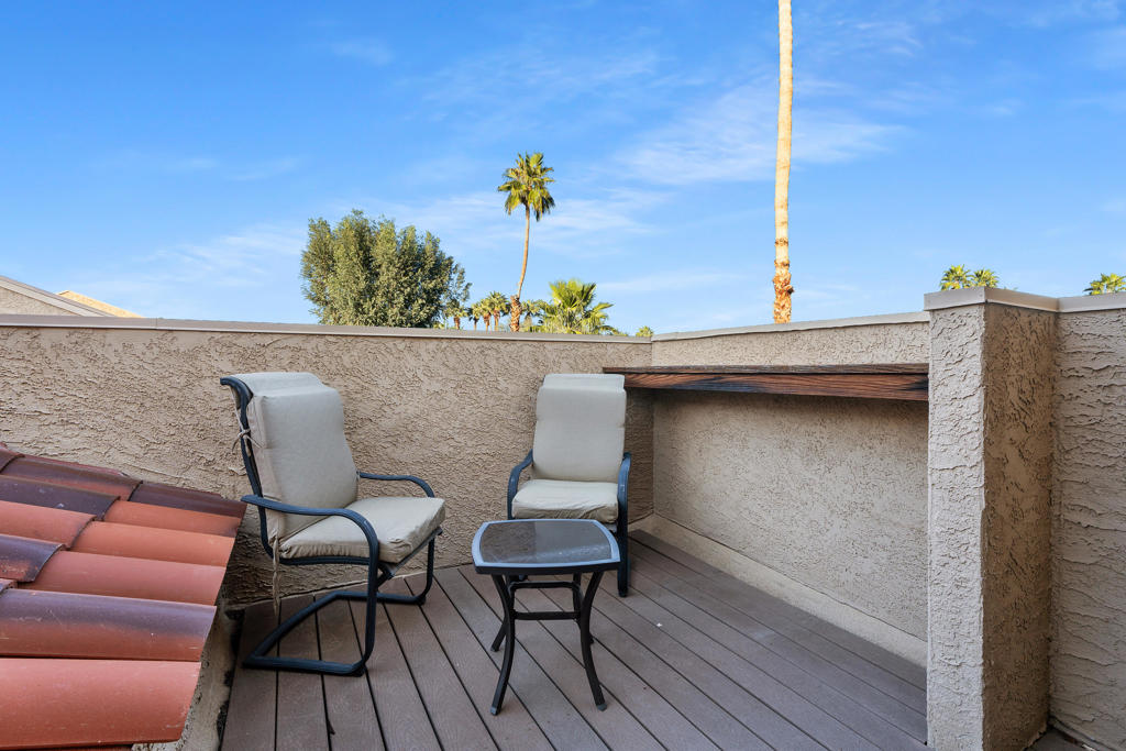 Rooftop patio with two cushioned chairs and a small table, enclosed by stucco walls with palm trees beyond.