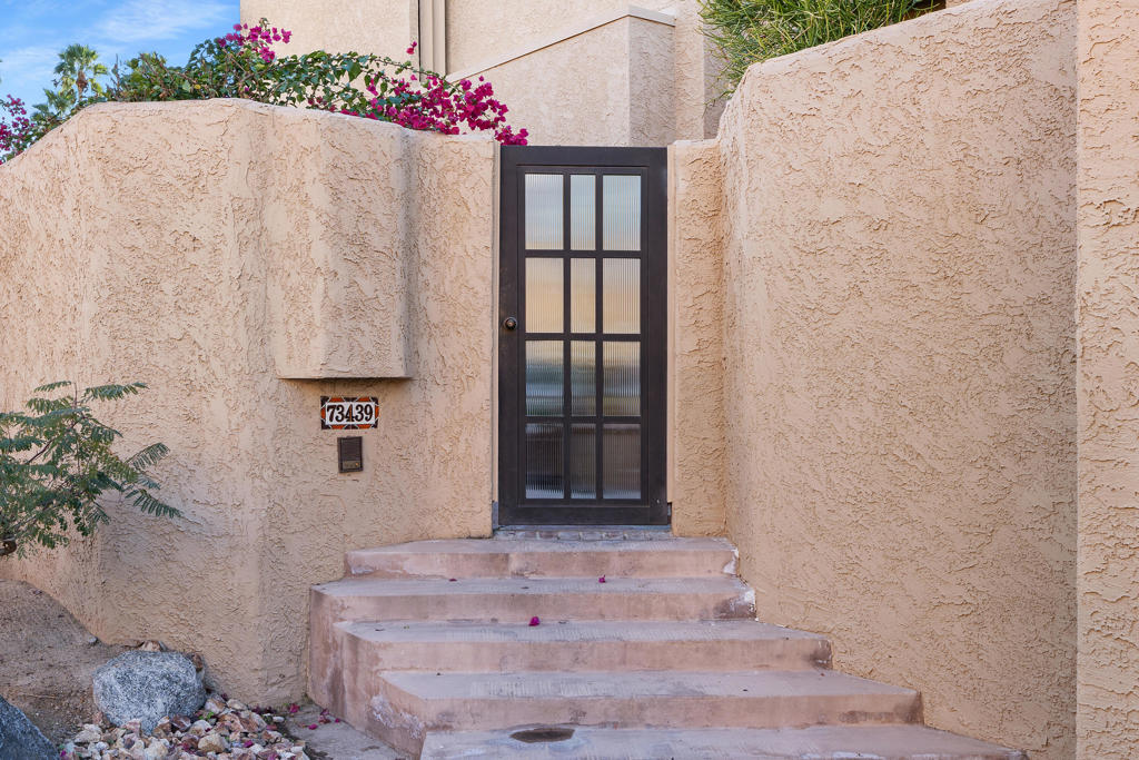 Stucco home entrance with a dark glass-paneled door, broad steps, and bougainvillea.
