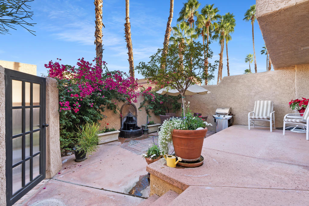 Enclosed courtyard patio with a fountain, flowering bougainvillea, potted plants, and seating.