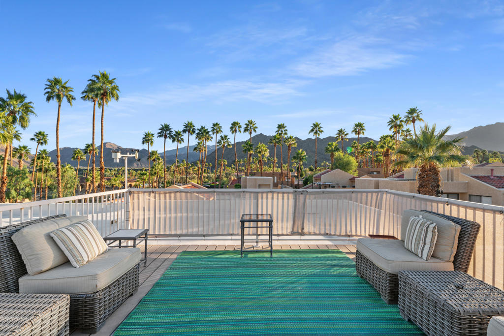 Rooftop patio with wicker seating and a teal rug overlooking palm trees and mountains.
