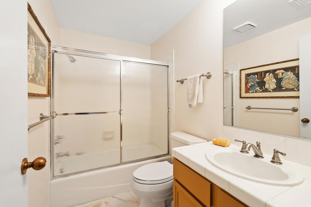Bathroom with a frosted-glass tub and shower, white tiled vanity, and large mirror.