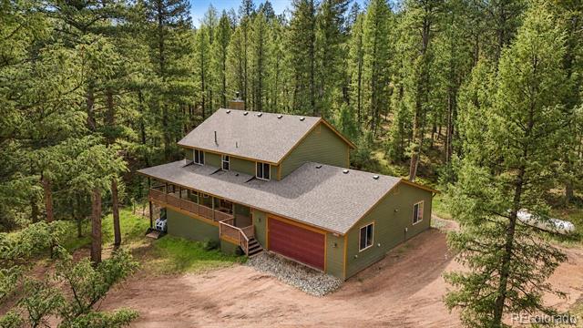 Aerial view of a green home with a red garage door and porch amid dense pine forest.