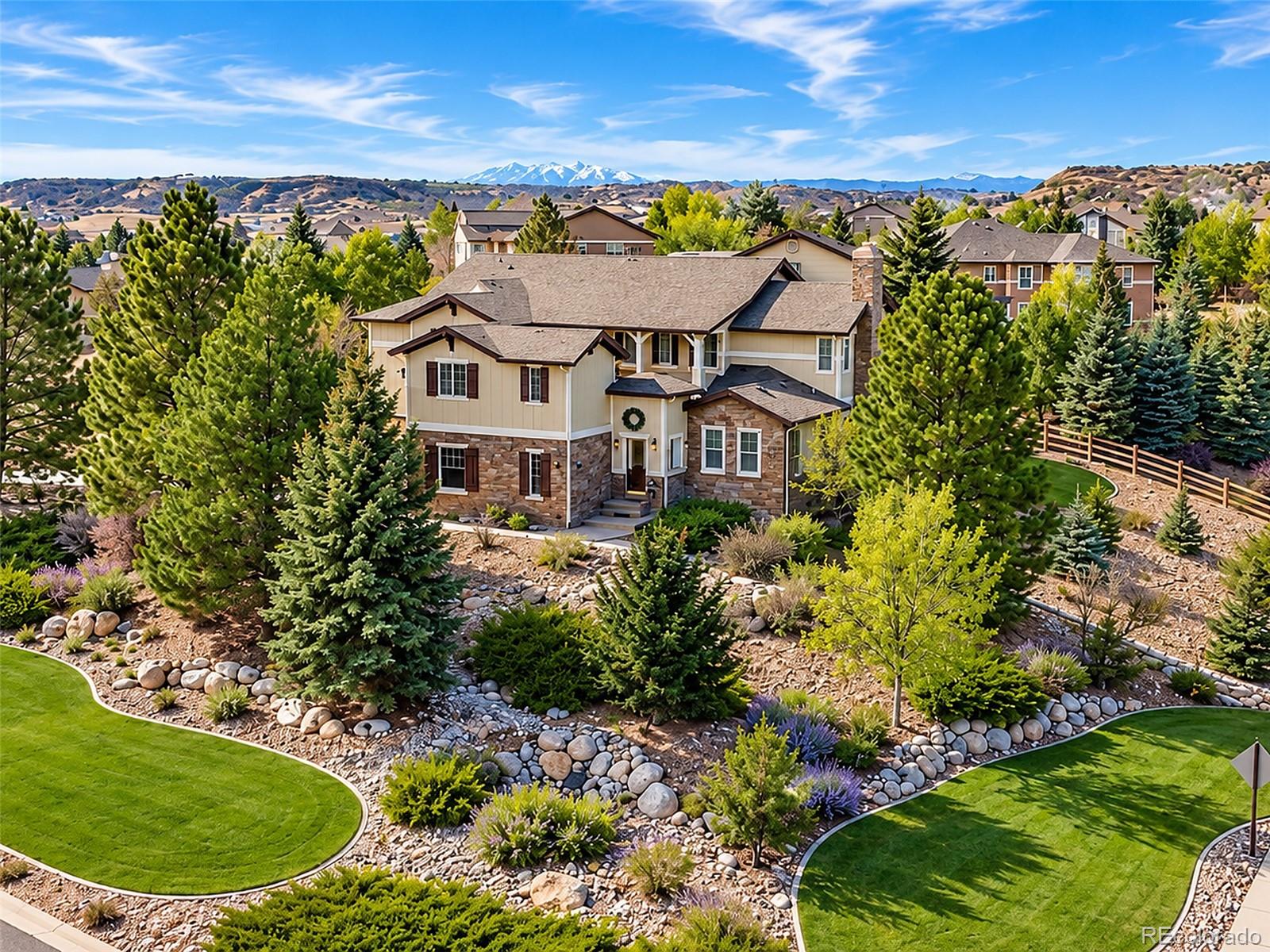 Two-story stone-and-siding home with landscaped gardens and snow-capped mountains in the distance.