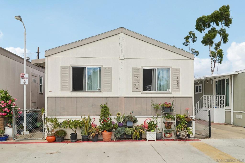 Manufactured home with a peaked roof, front windows, and rows of potted plants.