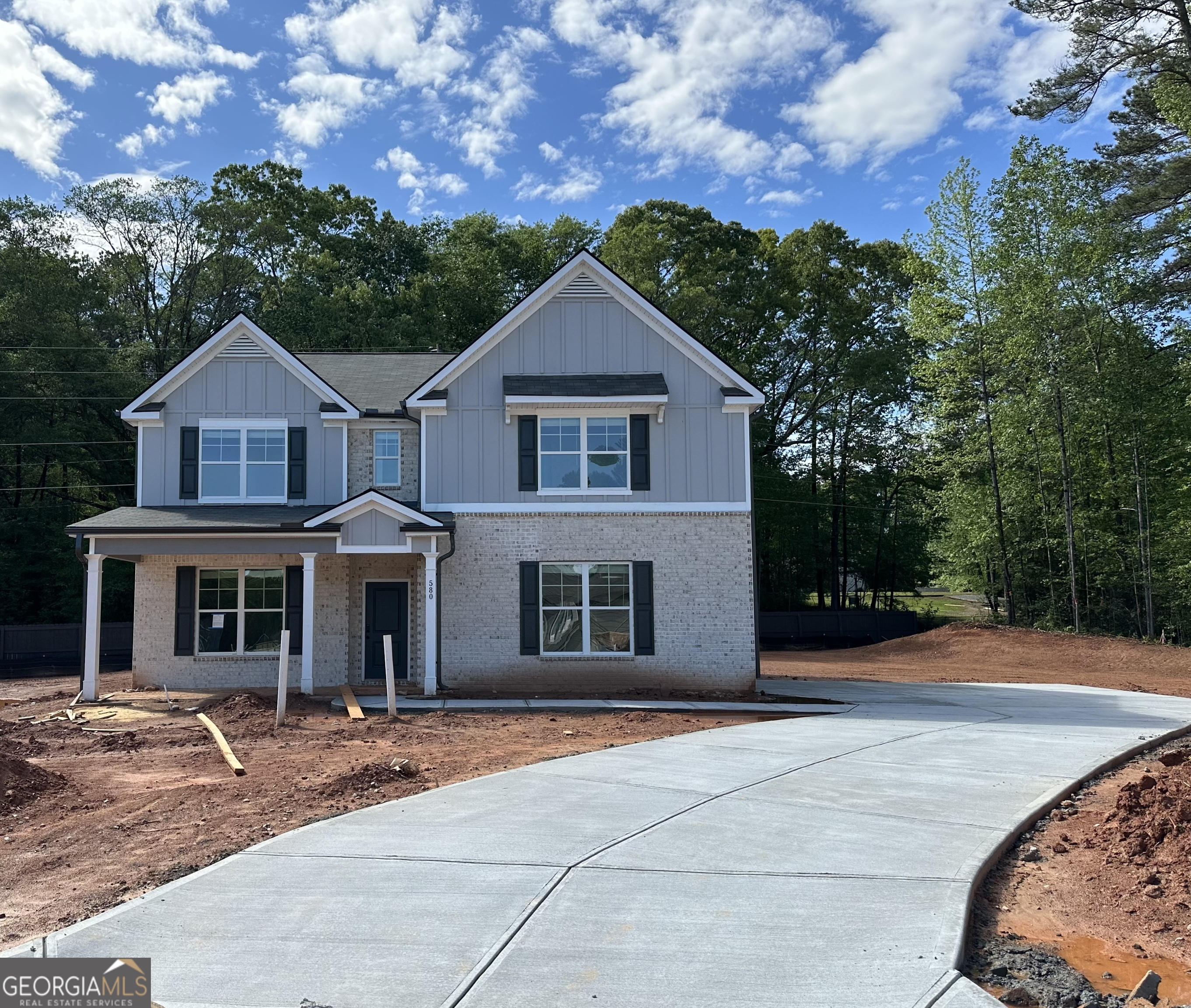 Two-story gray-and-brick house with dark shutters and a wide curved driveway amid unfinished landscaping.
