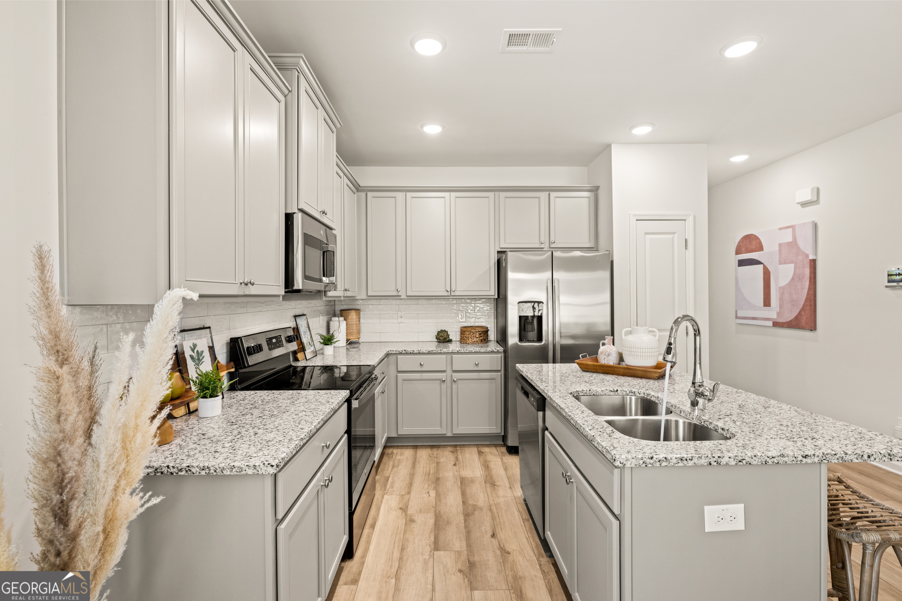 Staged kitchen with gray cabinets, granite counters, stainless steel appliances, and a large island sink.