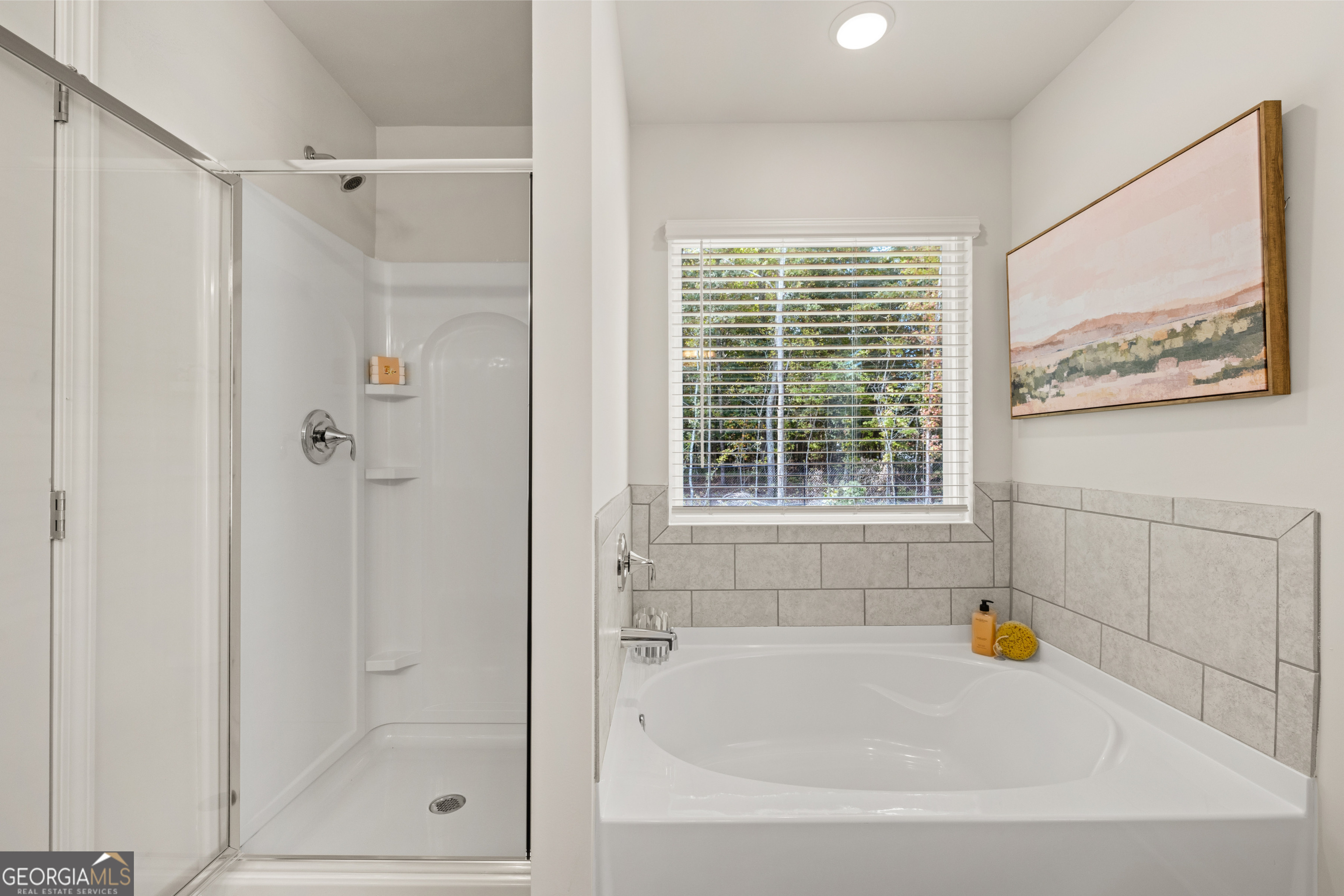 Bathroom with a built-in soaking tub beside a glass-enclosed shower and a window overlooking trees.