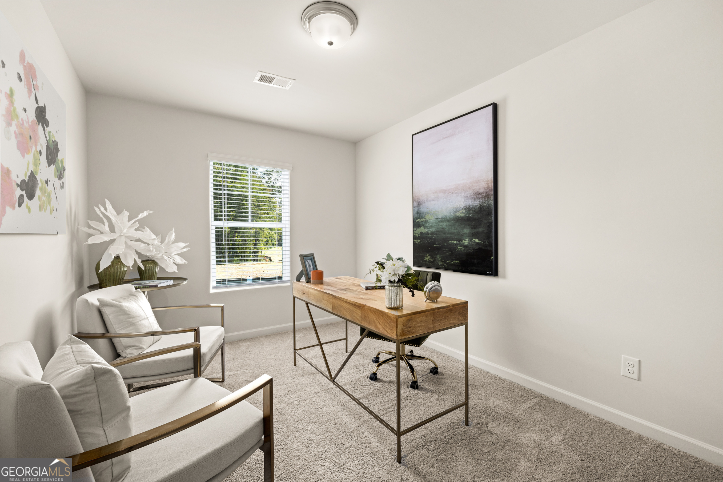 Staged home office with a wooden desk, white armchairs, and a large abstract painting.
