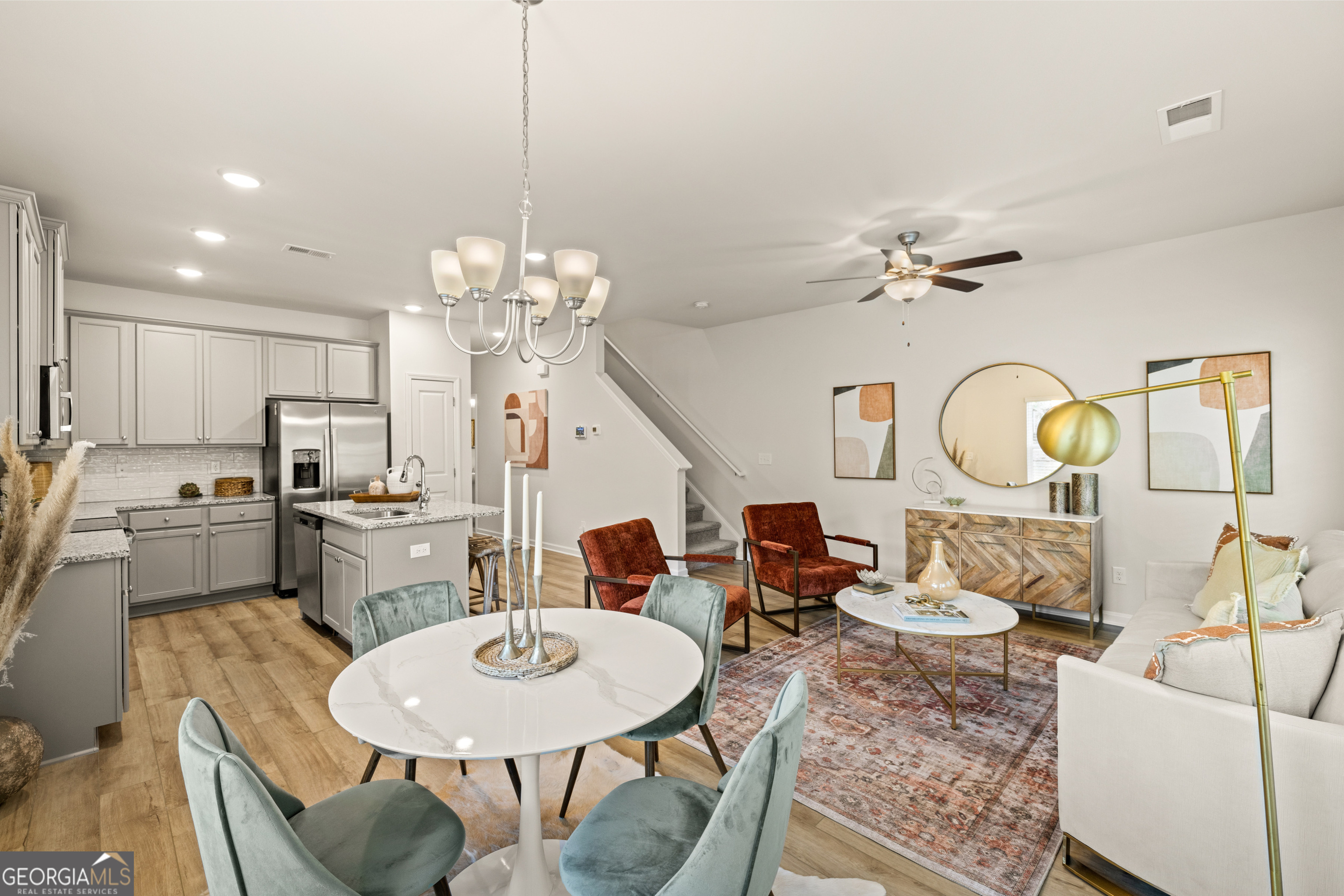 Open-plan living room and kitchen with gray cabinets, a round dining table, and rust-colored accent chairs.