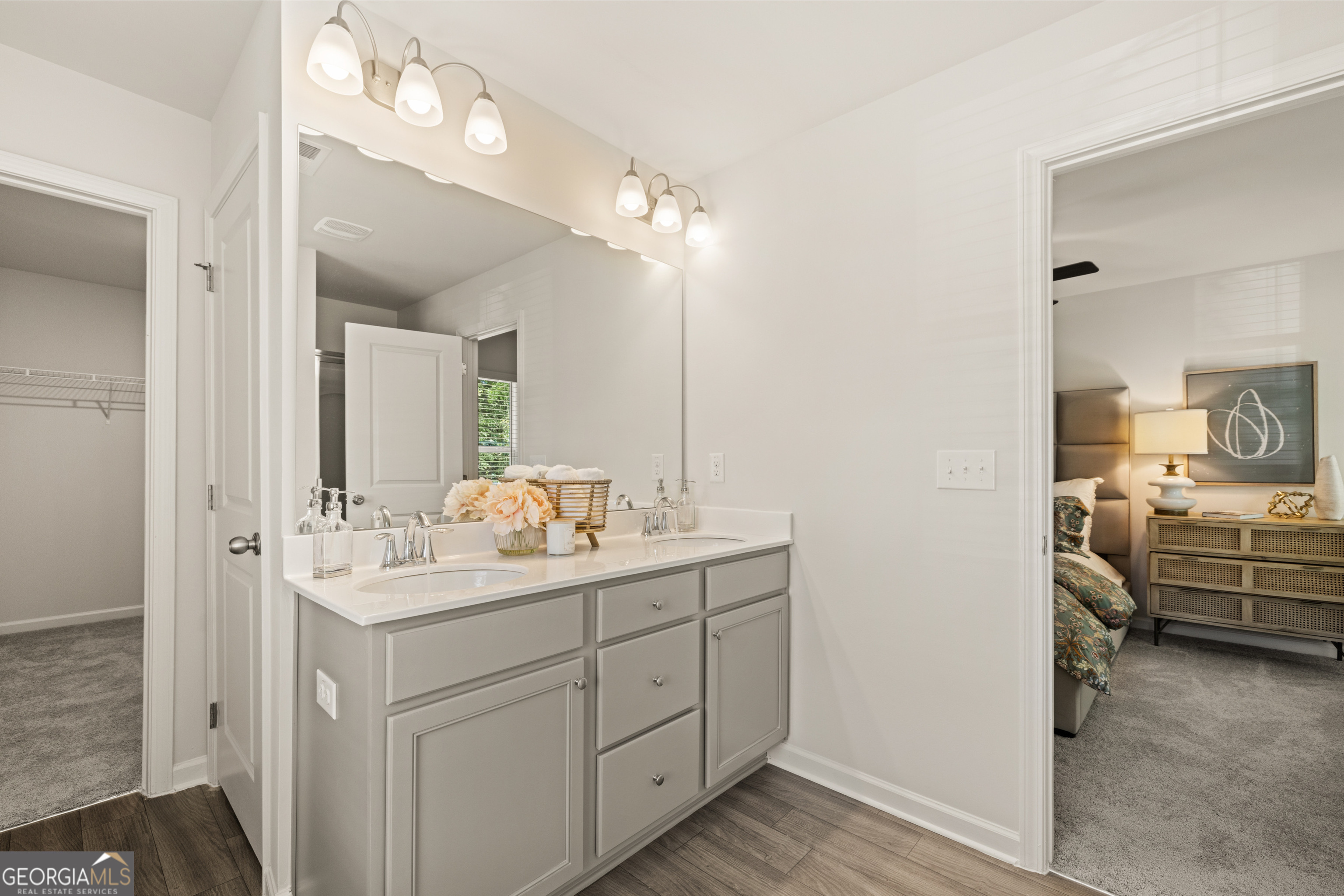 Bathroom with a gray double-sink vanity, large mirror, and open views into a closet and bedroom.