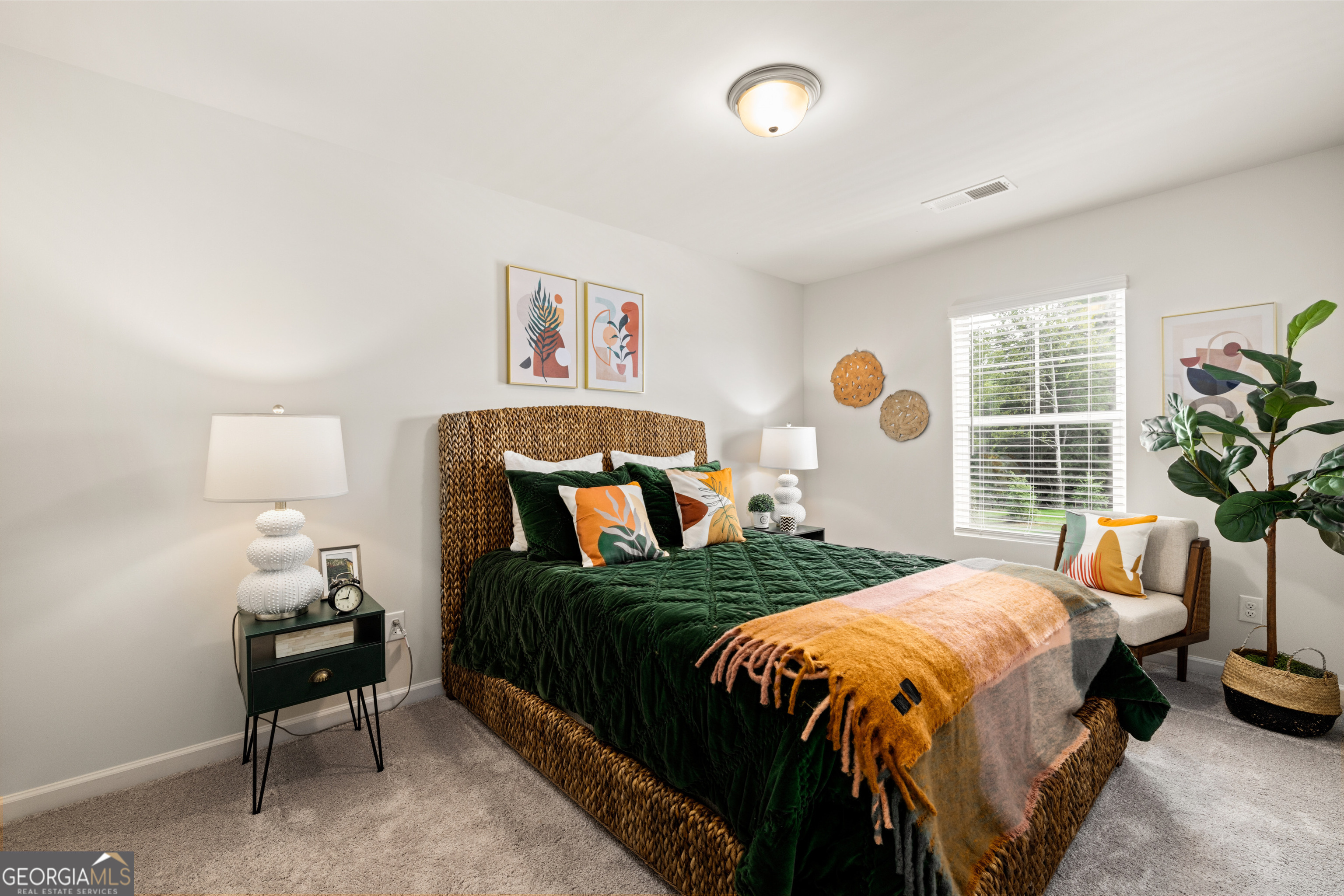 Staged bedroom with a woven bed frame, deep green bedding, and colorful pillows.