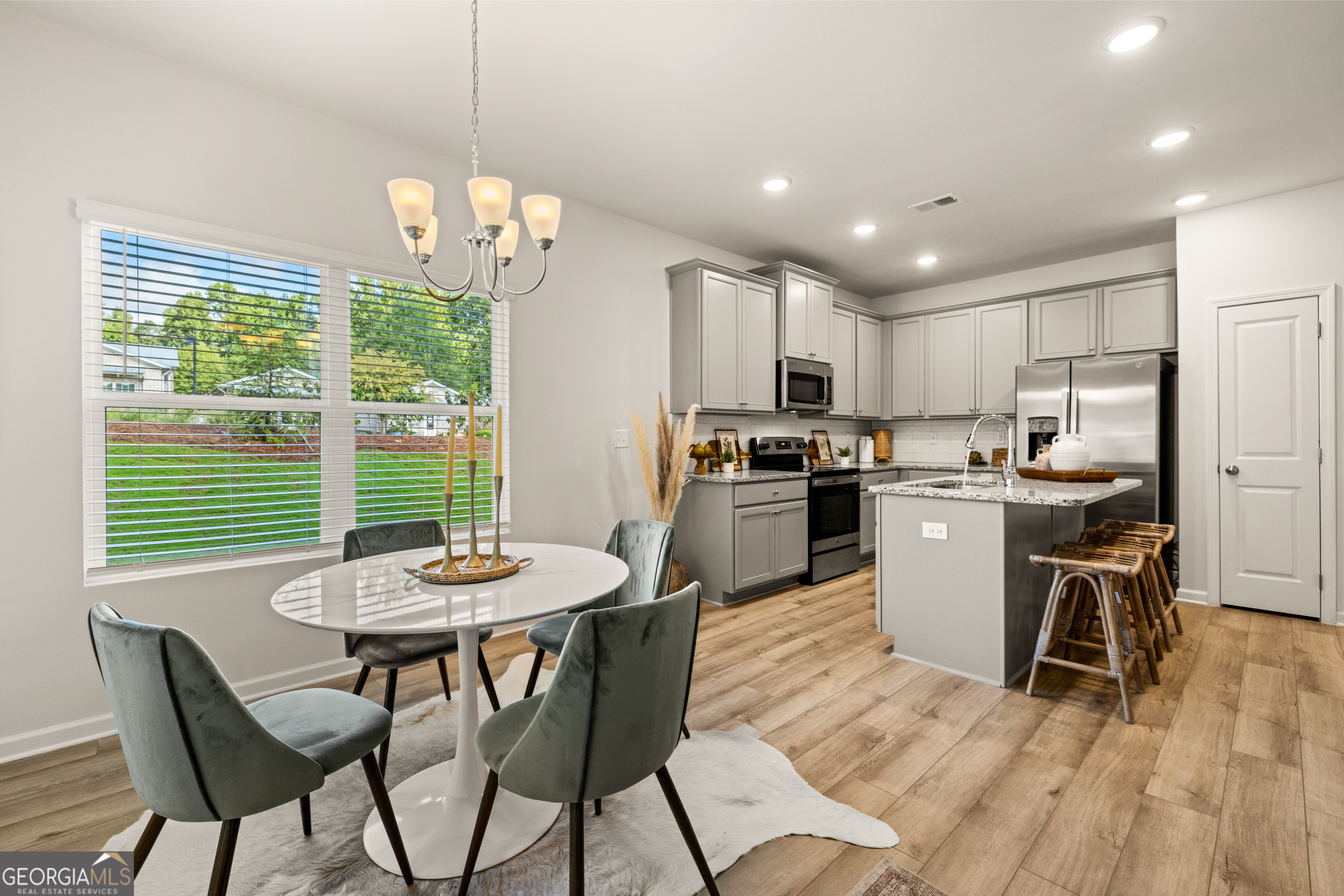 Open kitchen and dining area with gray cabinets, stainless steel appliances, and a large island with bar stools.