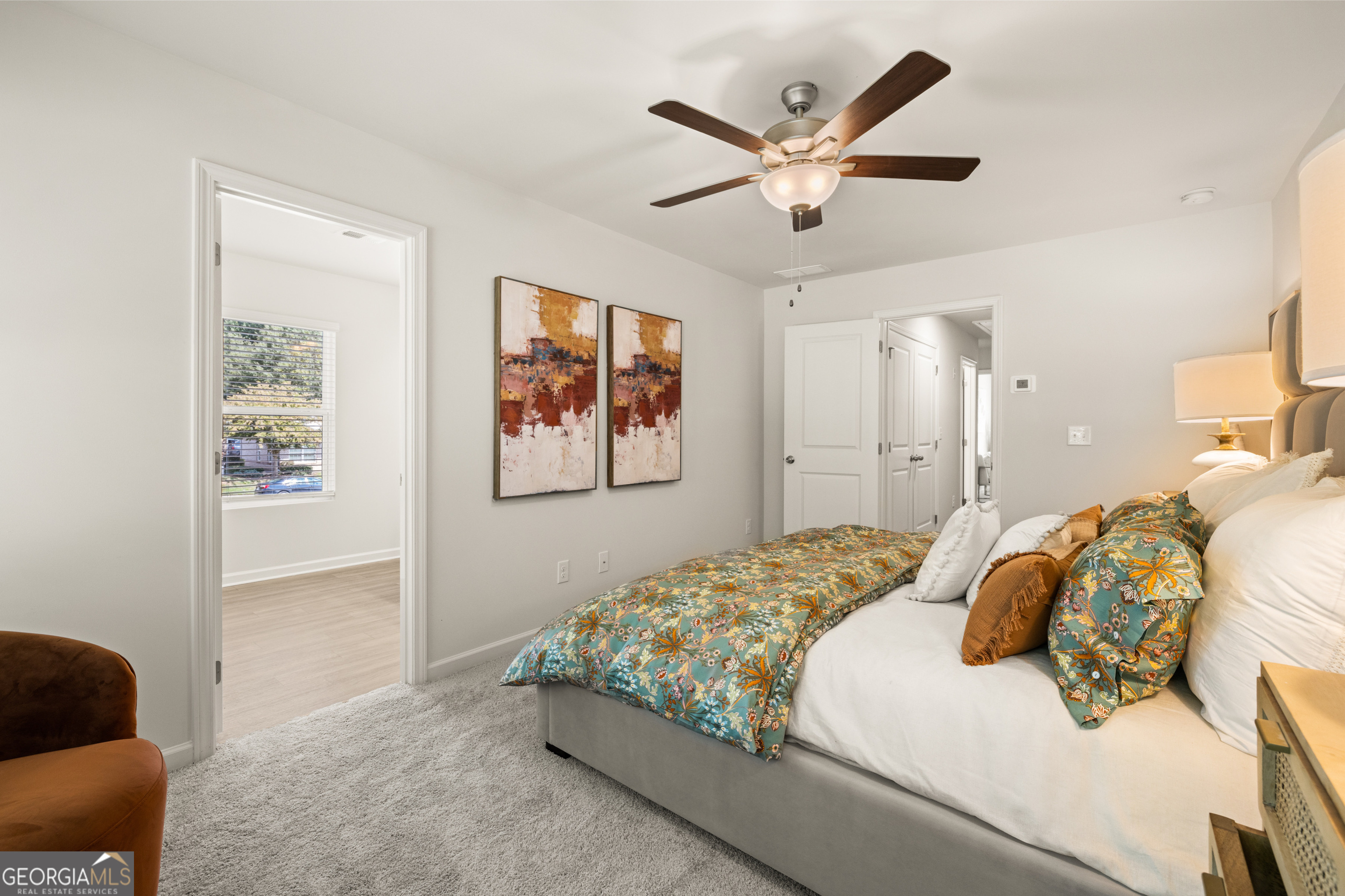 Furnished bedroom with a teal floral comforter, abstract wall art, and a lit ceiling fan.