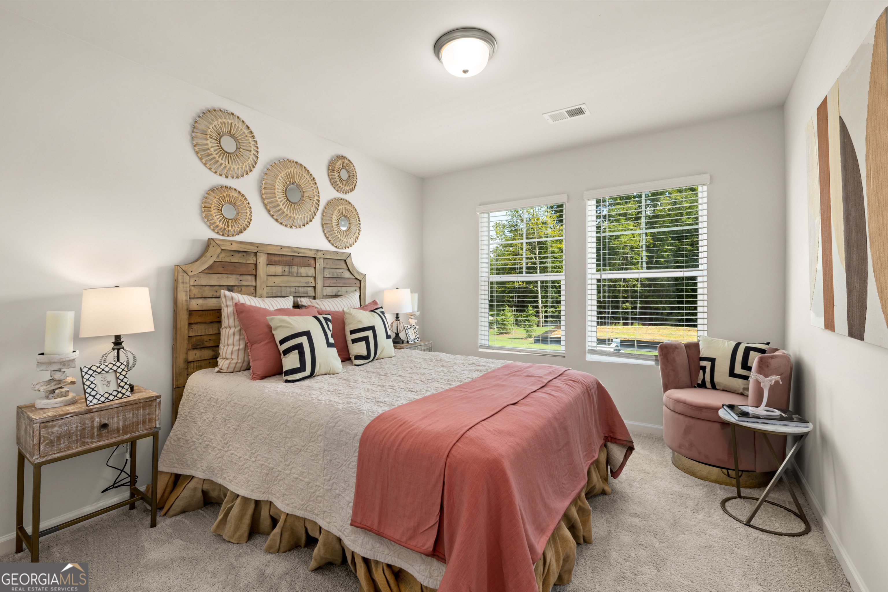 Furnished bedroom with a rustic wood headboard, blush bedding, and windows overlooking trees.