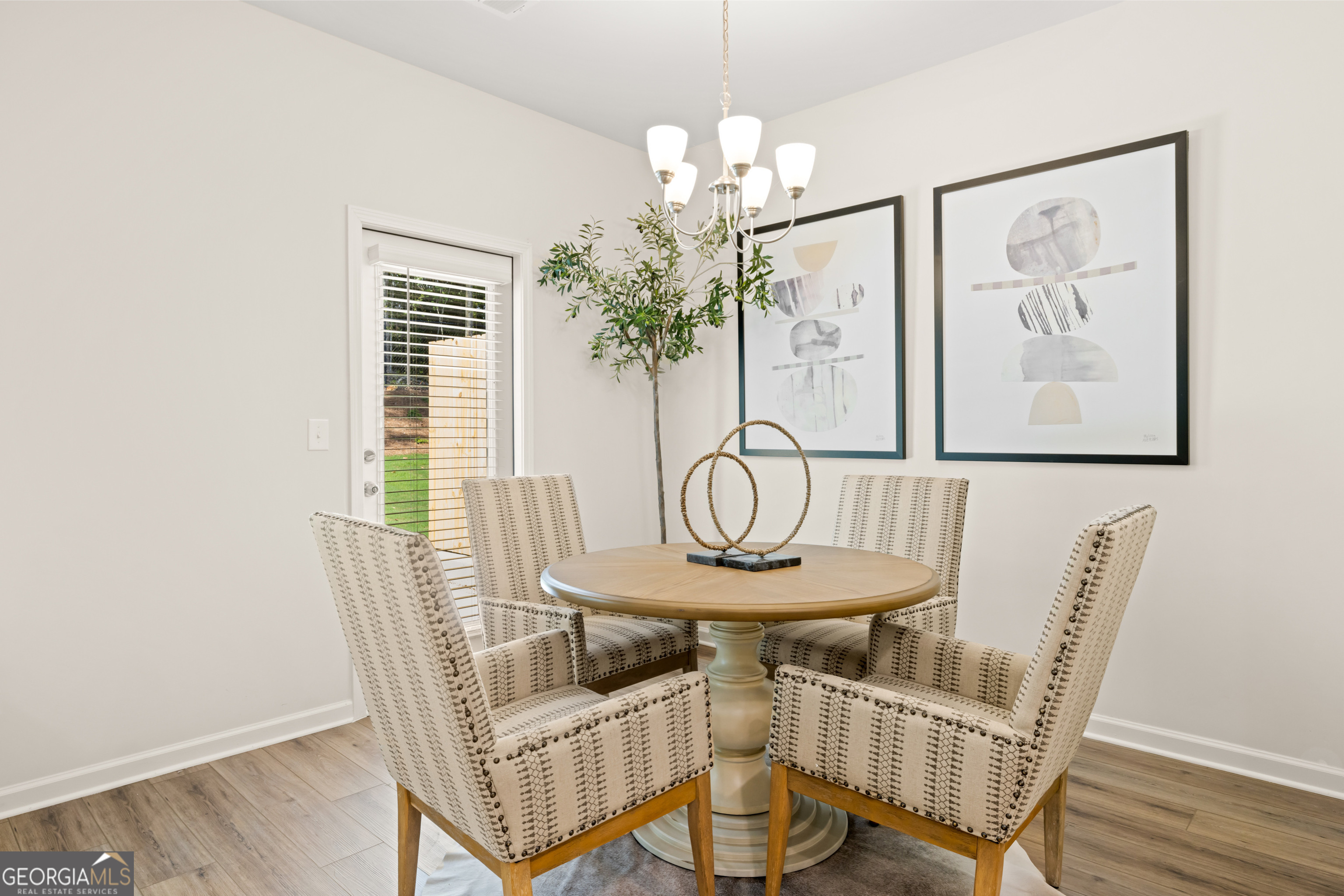 Dining area with a round pedestal table, four patterned chairs, chandelier, and framed abstract art.