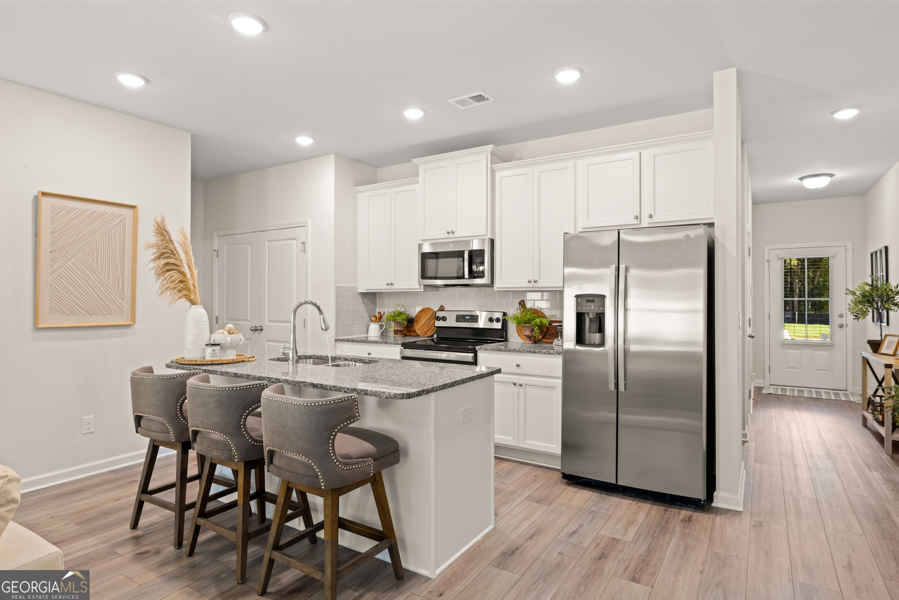 Bright kitchen with white cabinets, stainless steel appliances, and a granite island with three stools.