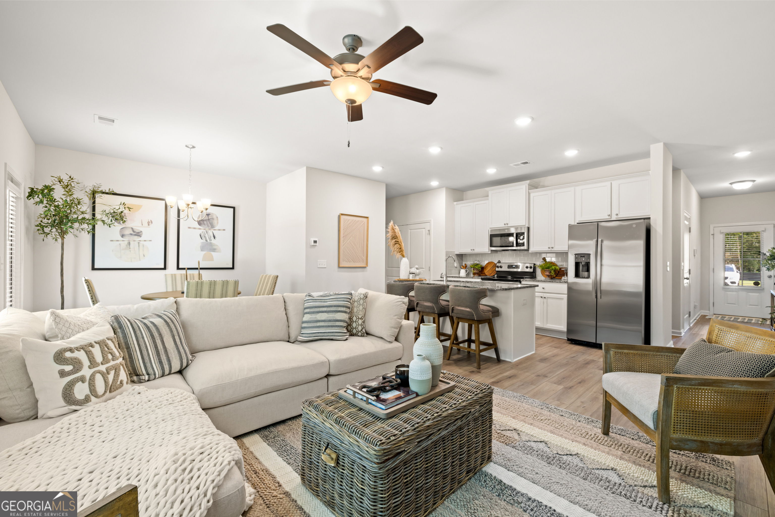 Open-plan living room and kitchen with a cream sectional, woven coffee table, and white cabinetry.