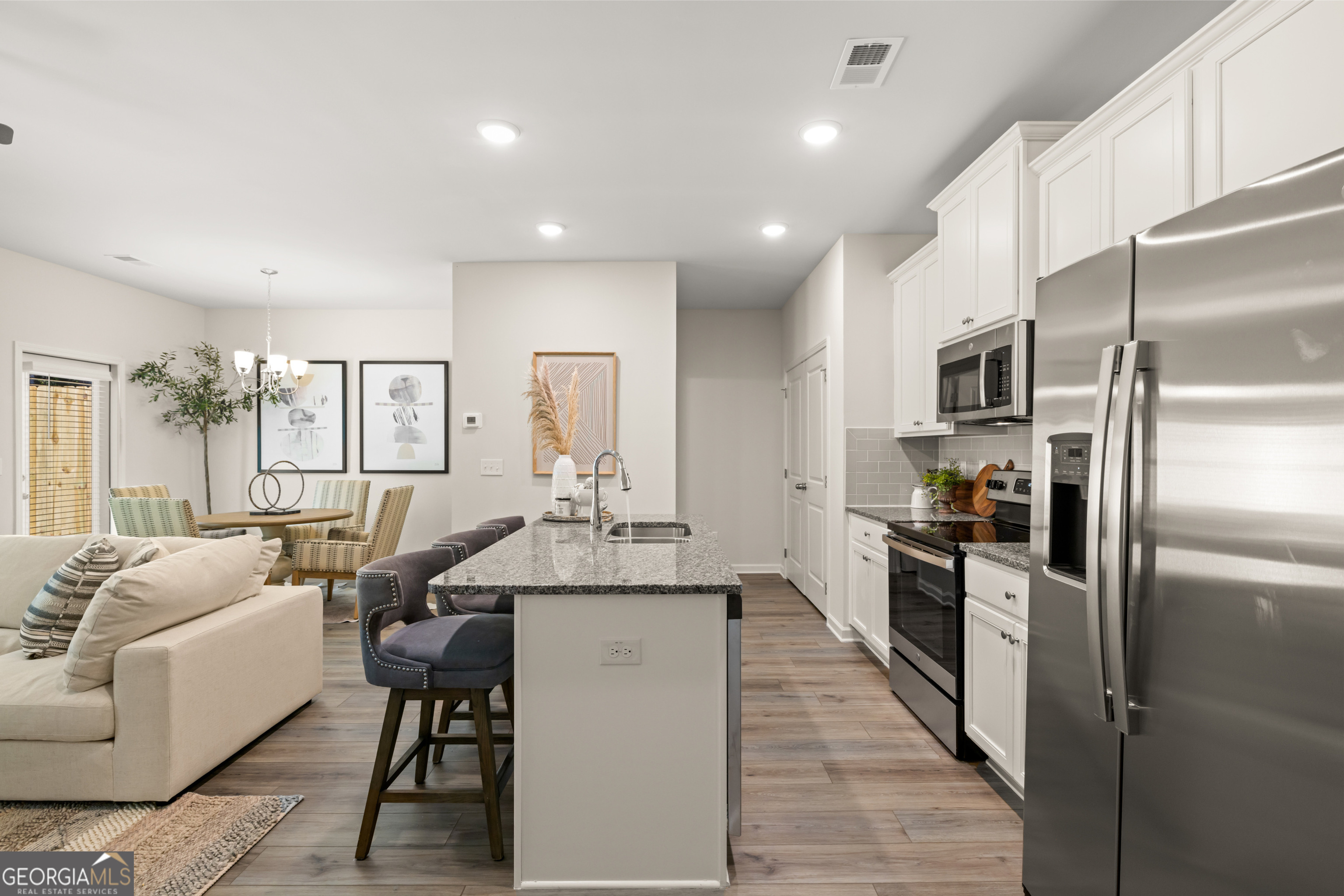 Open kitchen with a gray stone island, white cabinets, stainless steel appliances, and an adjoining dining and living area.