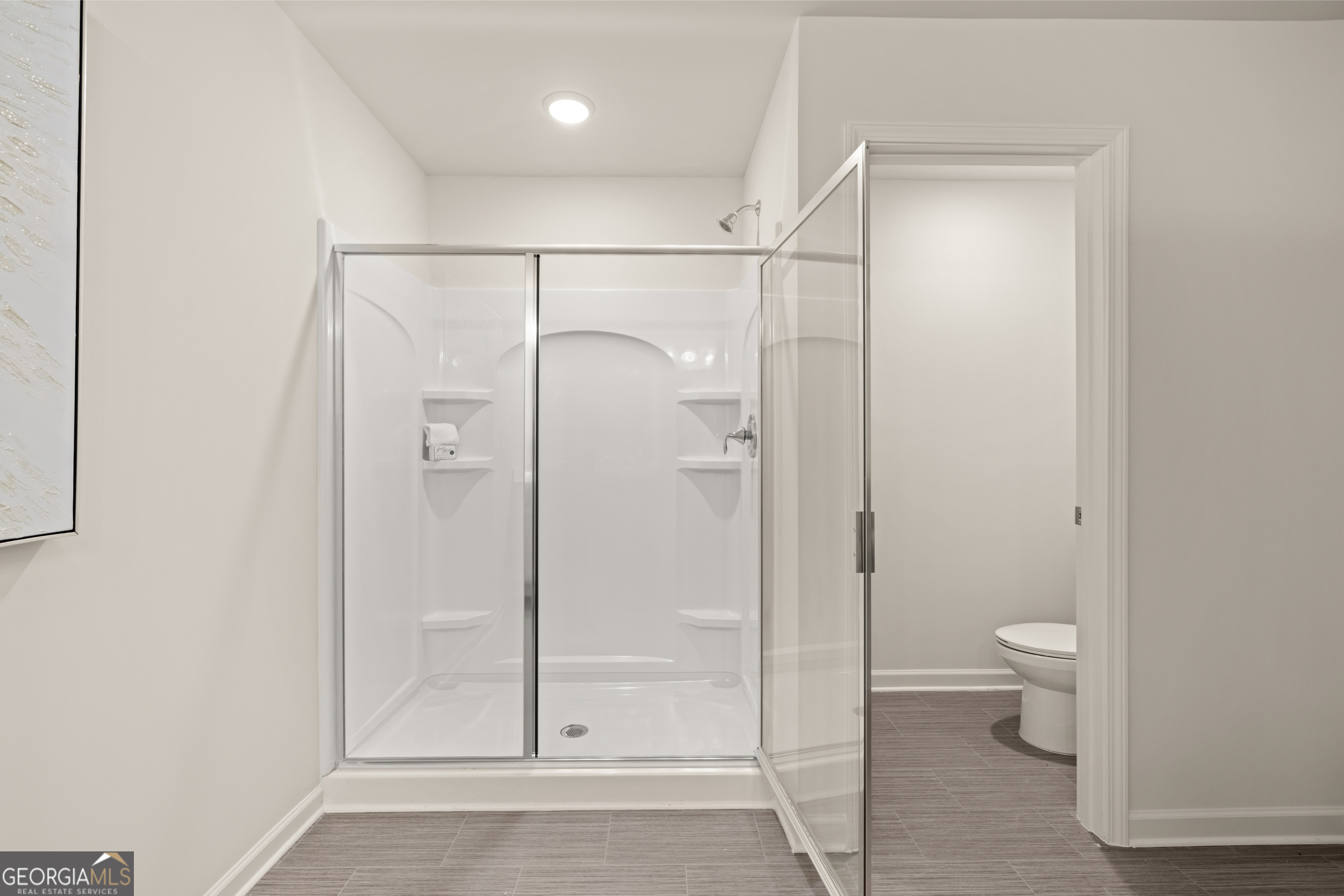 Bathroom with a spacious glass-enclosed shower and toilet visible through the doorway.