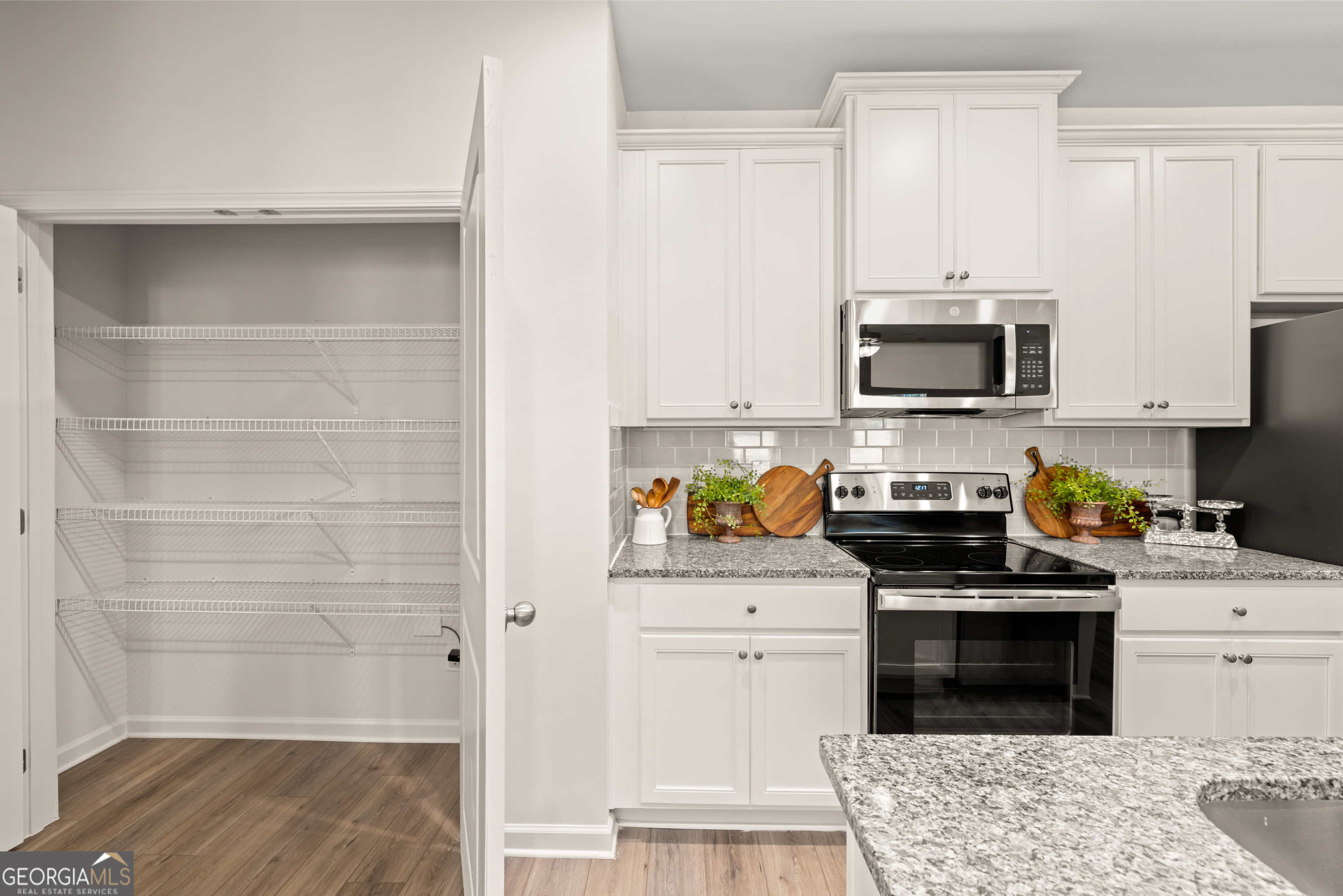 Kitchen with white cabinets, stainless steel appliances, granite counters, and an open wire-shelved pantry.
